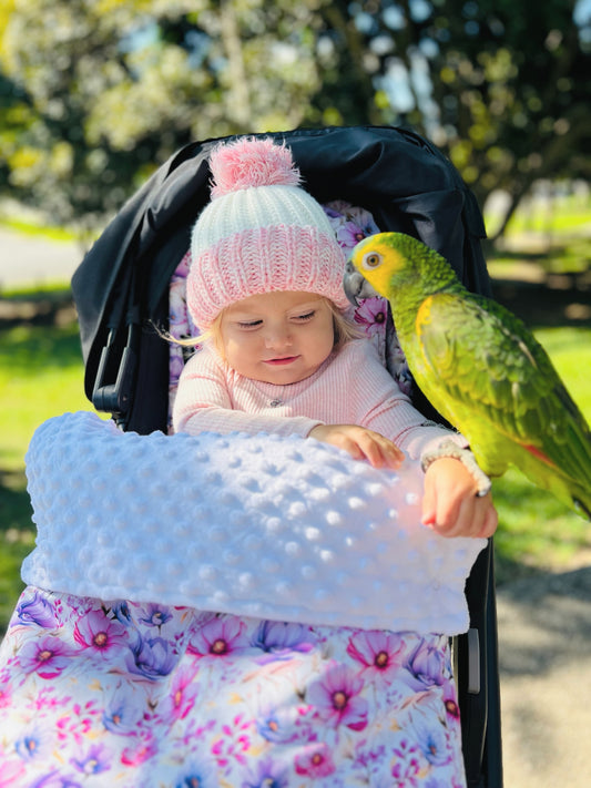 Baby girl in a pram footmuff staying warm and cosy in a Harmony J design.